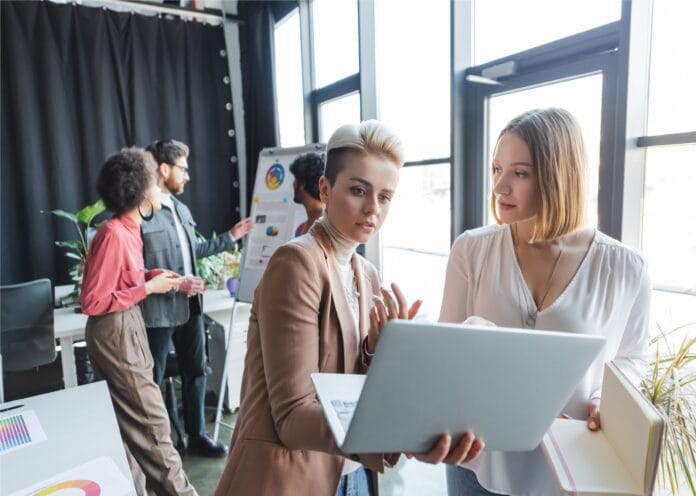 advertising managers talking near laptop and multiethnic colleagues near flip chart on background.