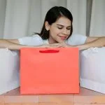 Uśmiechnięta kobieta w domu otoczona kolorowymi torbami zakupowymi